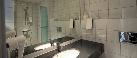 A modern bathroom with two sinks, a glass shower enclosure, and a mirror with a towel rack.