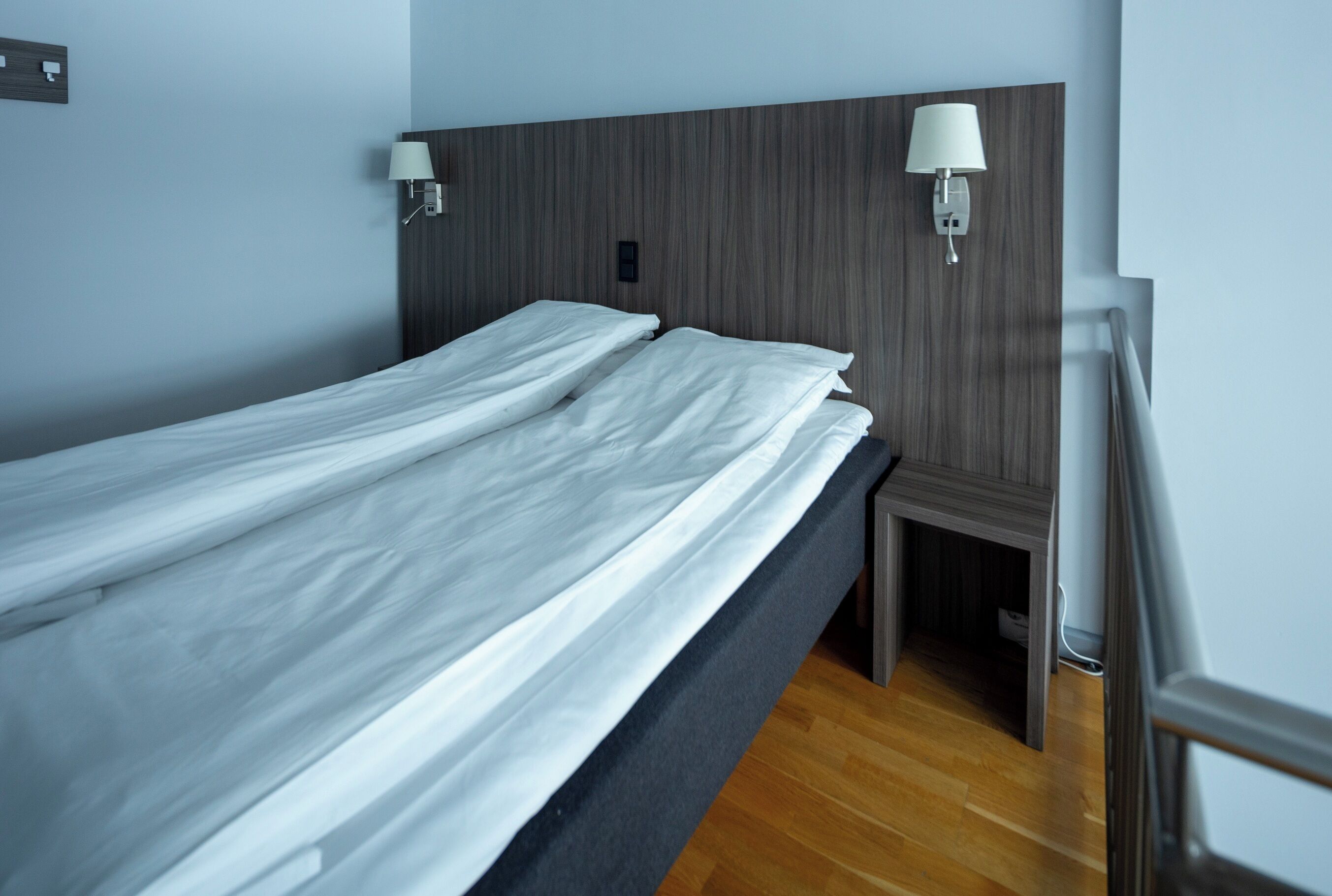 A neatly made bed with white linens in a room with wooden paneling on the walls and a wooden floor.