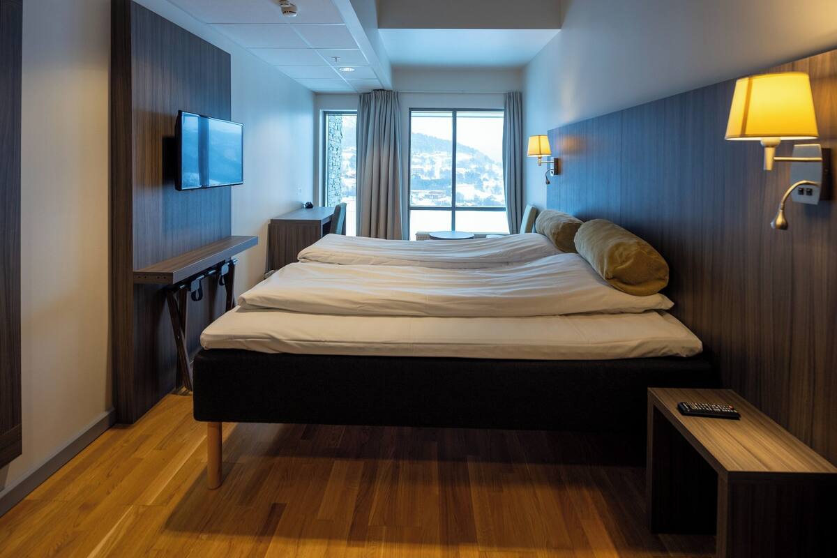Ein Hotelzimmer mit einem großen Bett, einem Schreibtisch mit Stuhl, einem an der Wand montierten Fernseher und einem Fenster mit Bergblick.