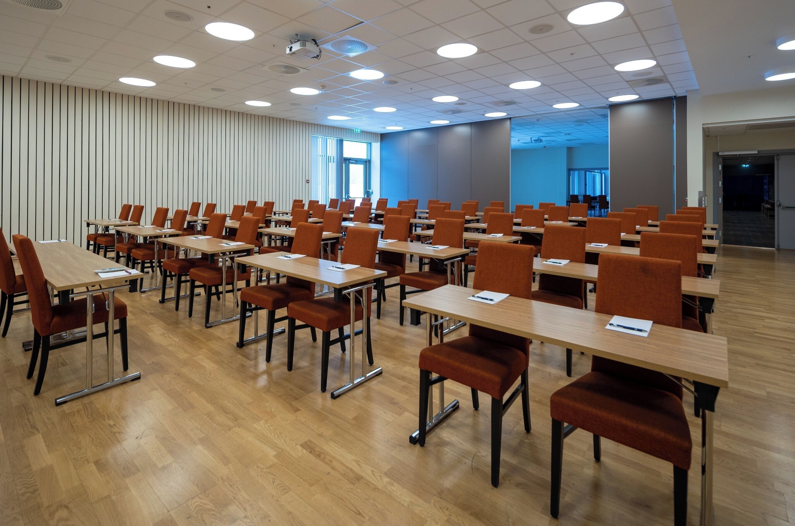 Une salle de conférence avec des rangées de tables et de chaises, de grandes fenêtres et un design moderne au niveau du plafond.