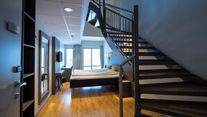 Ein modernes Hotelzimmer mit Holzboden, einem Bett, einem Schreibtisch und einer Treppe.