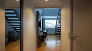 Ein modernes Interieur mit Holzboden, einer Essecke mit Tisch und Stühlen, einer Couch und einer Treppe, die in eine obere Ebene führt.
