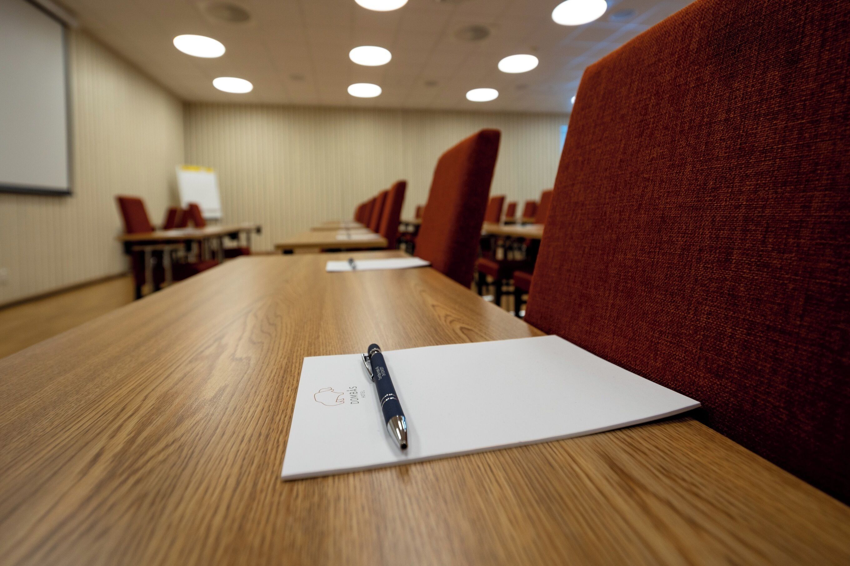 A conference room with a long table, red upholstered chairs, and a whiteboard on the wall.