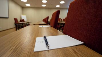 A conference room with a long table, red upholstered chairs, and a whiteboard on the wall.