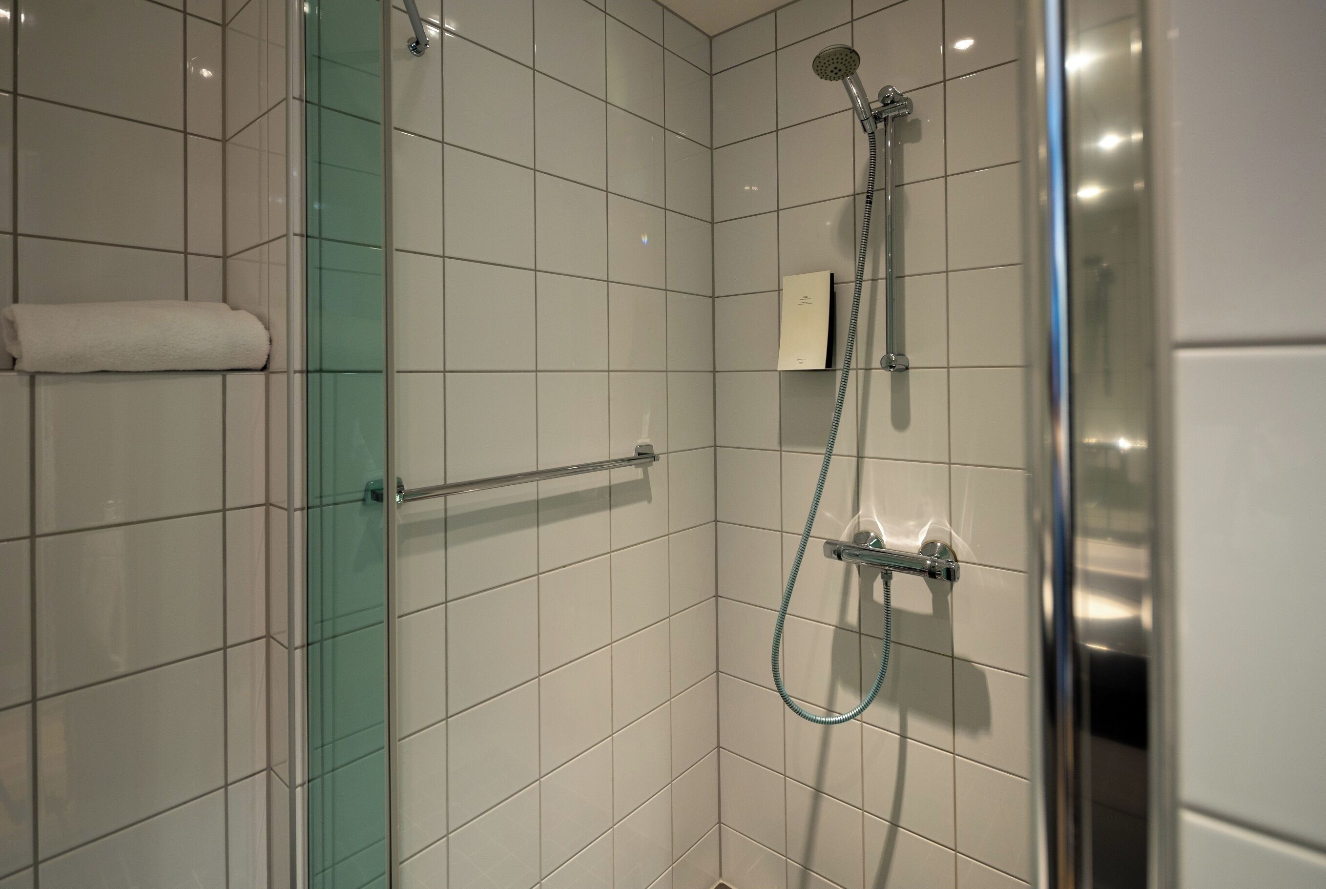 Una doccia moderna con porta in vetro, porta asciugamani e soffione a mano.