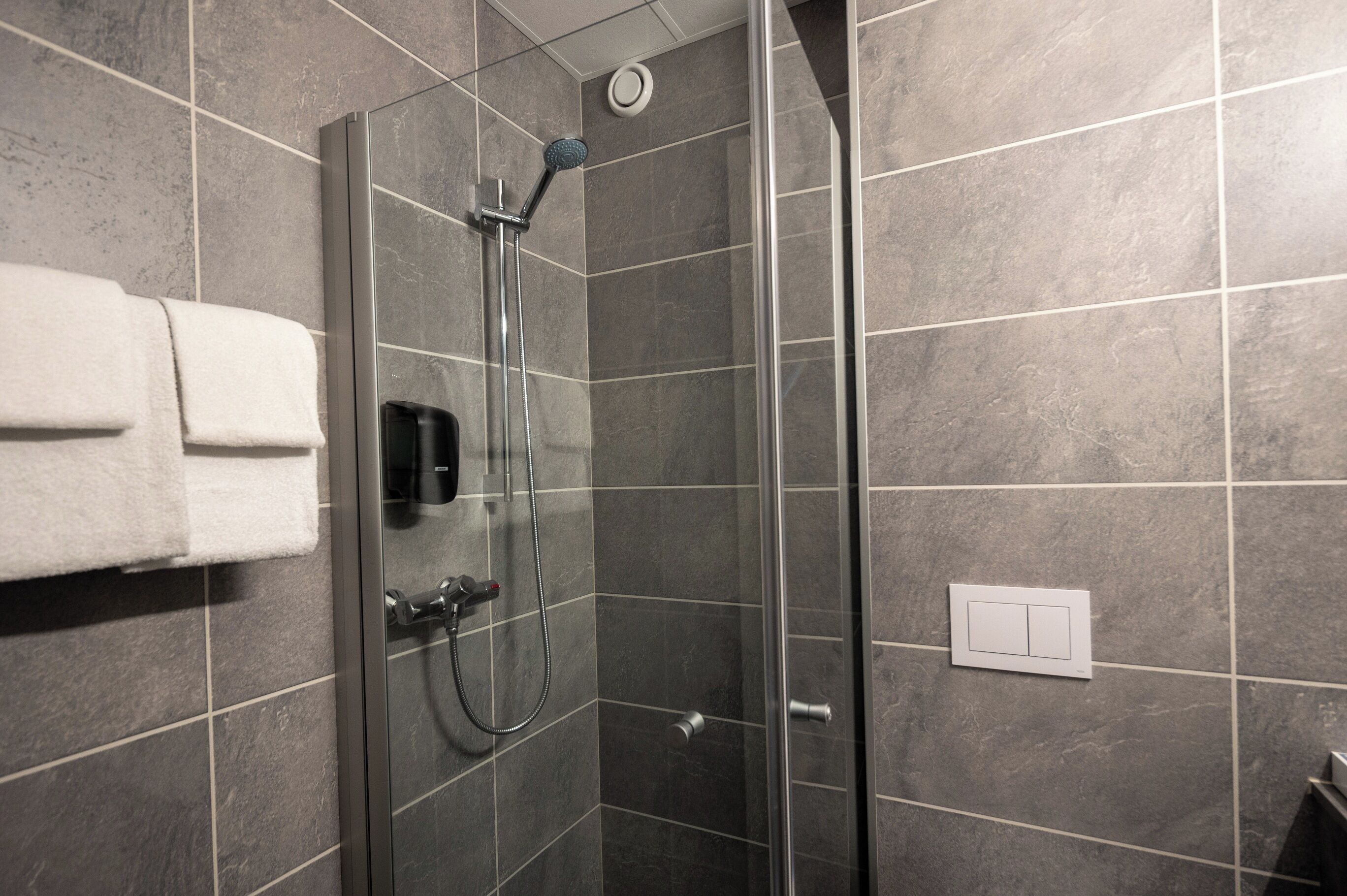 A modern shower with a handheld showerhead, a glass door, and a towel rack with a white towel.