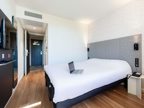 Une chambre d’hôtel moderne avec un grand lit, un bureau avec un ordinateur portable, un téléphone et une télévision.