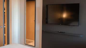 Ett hotellrum med en säng, en garderob, en spegel, en tv som är monterad på väggen och en fjärrkontroll som ligger på sängen.