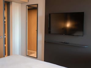 Een hotelkamer met een bed, een kledingkast, een spiegel, een aan de muur bevestigde televisie en een afstandsbediening op het bed.