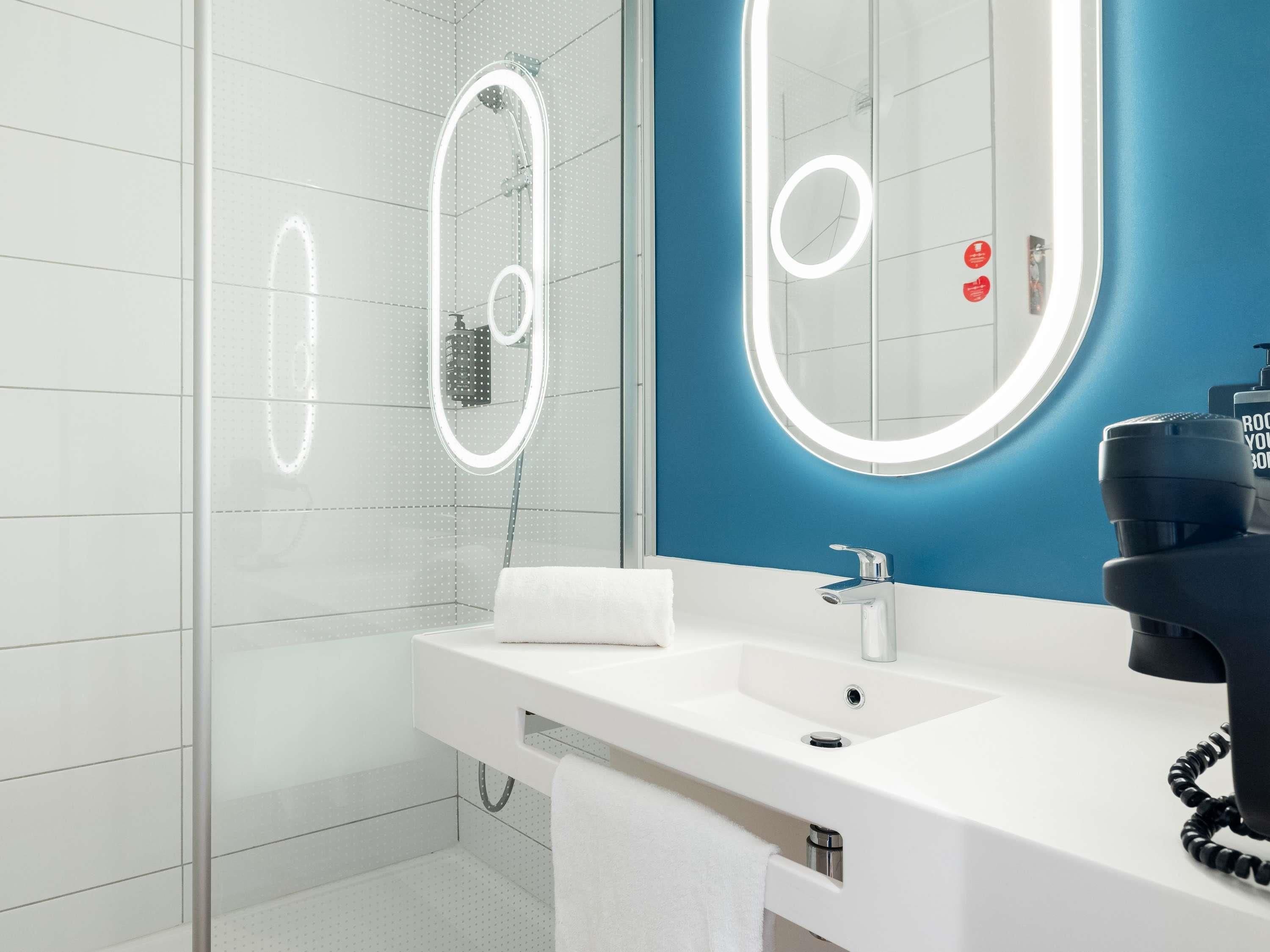 Un baño moderno con cabina de ducha de vidrio, un lavabo blanco con espejo y una pared de acento azul.