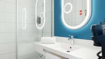 Un baño moderno con cabina de ducha de vidrio, un lavabo blanco con espejo y una pared de acento azul.