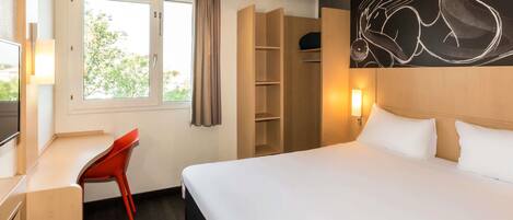 A hotel room with a bed, a desk, a chair, a wardrobe, and a window with curtains.