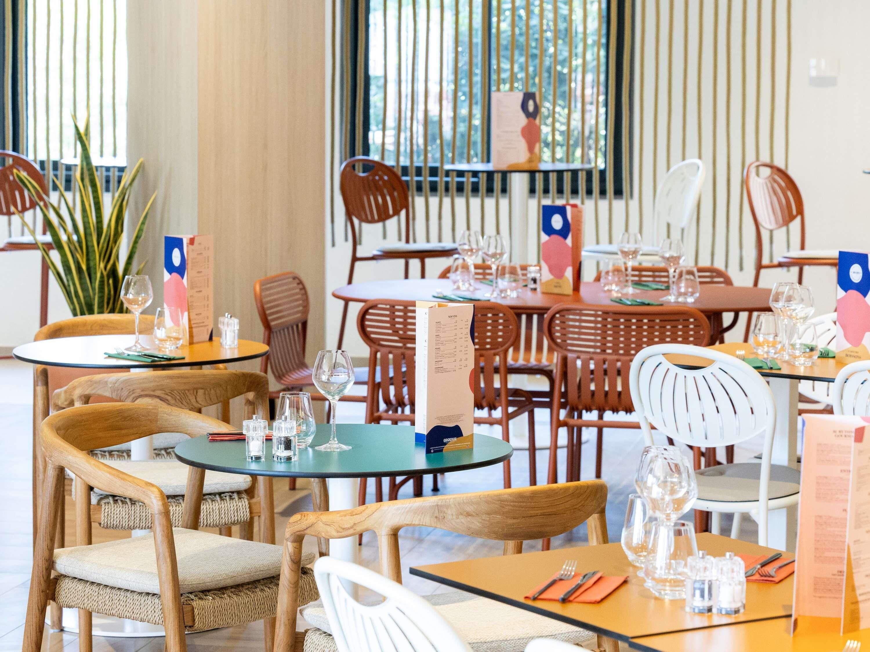 Ein Restaurantinneres mit mehreren Tischen, Stühlen, Speisekarten und Weingläsern.