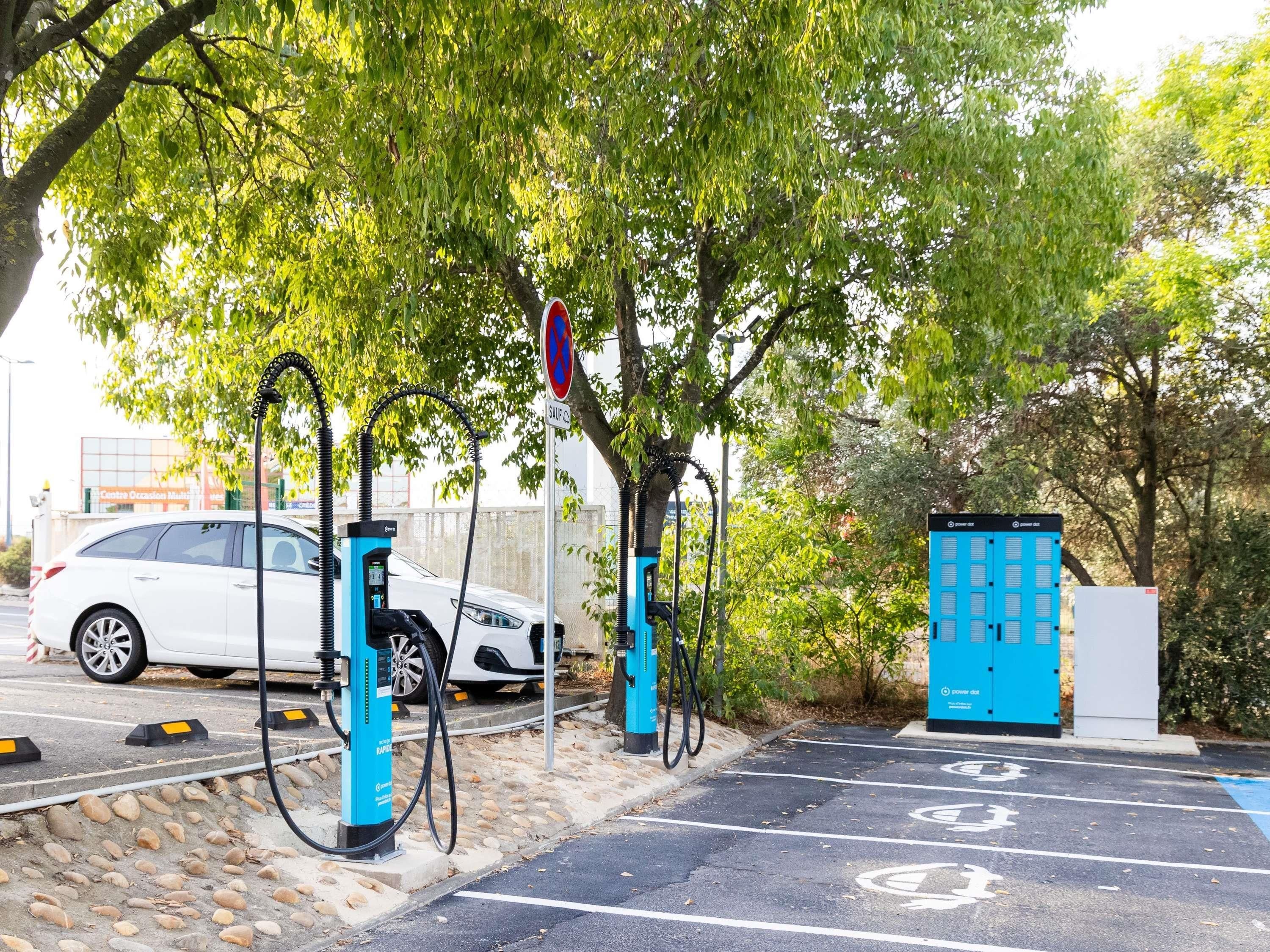 A parking area with electric vehicle charging stations, a white car, and a blue energy storage unit.