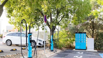 A parking area with electric vehicle charging stations, a white car, and a blue energy storage unit.