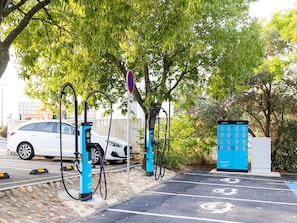 Een parkeerplaats met oplaadpunten voor elektrische voertuigen, een witte auto en een blauwe energieopslagunit.