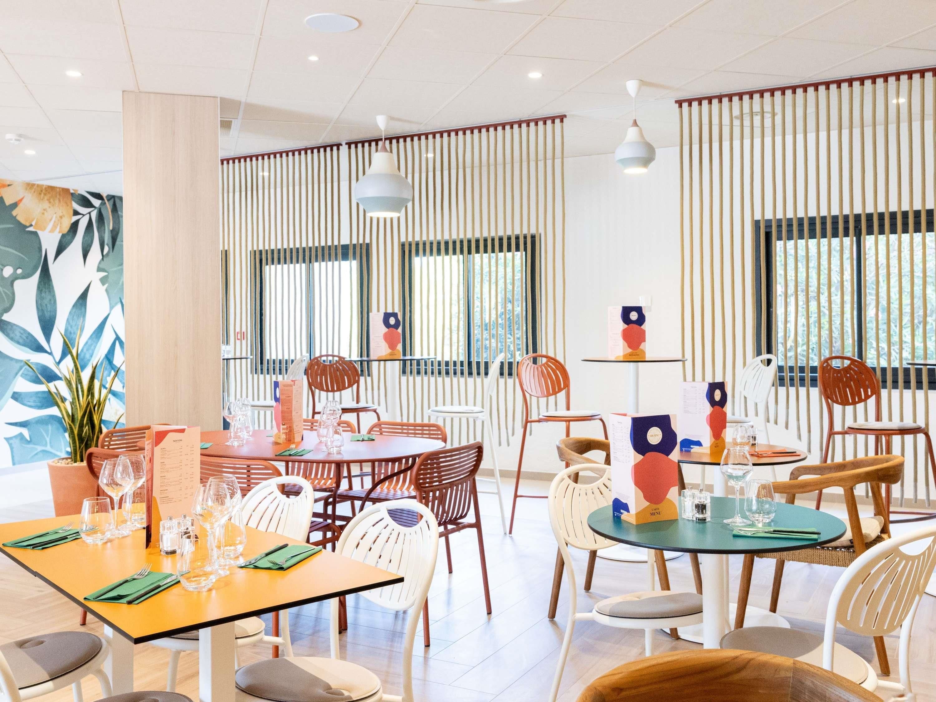 Un comedor moderno con varias mesas y sillas, un atril para el menú y persianas verticales en las ventanas.