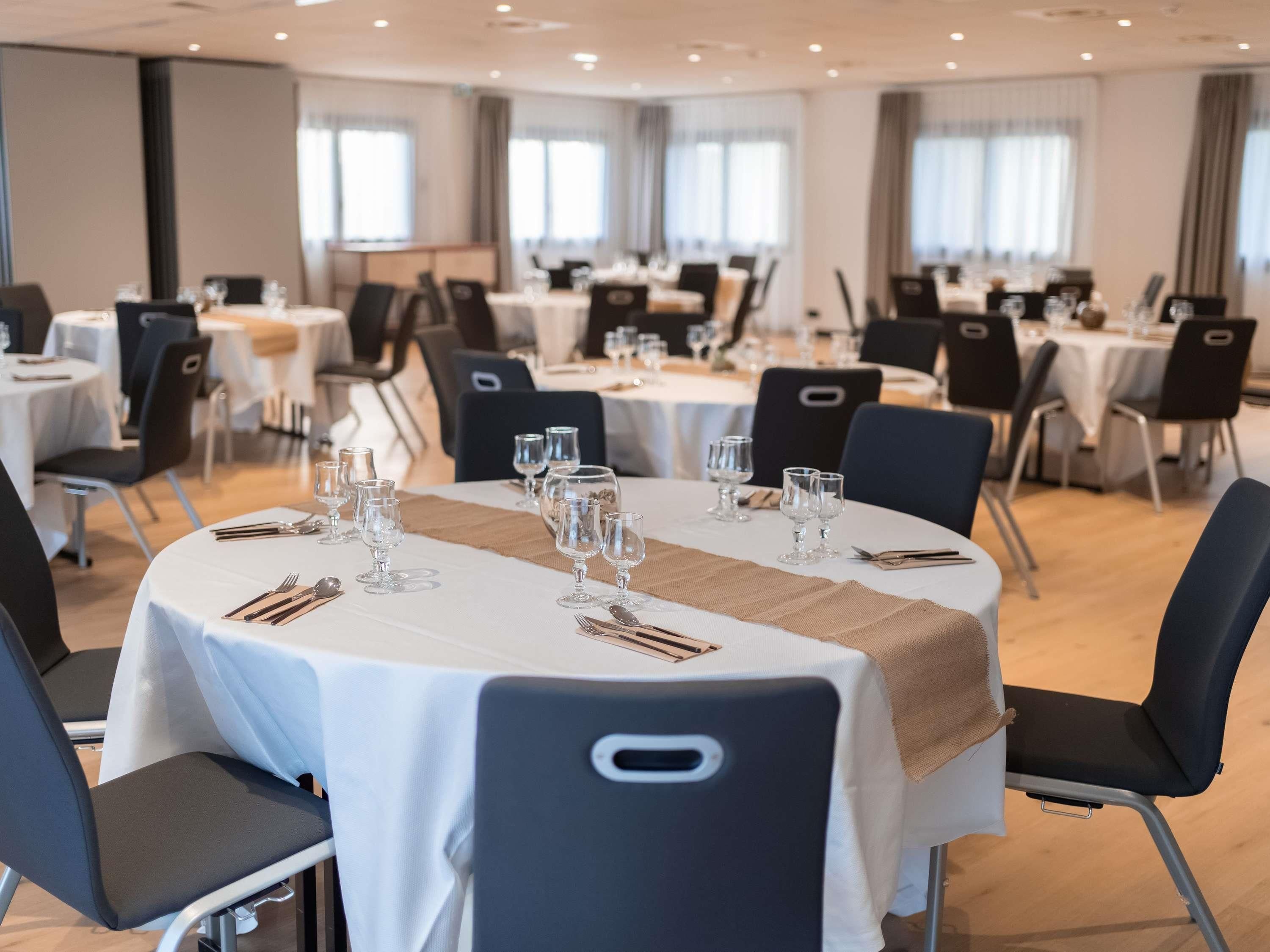 A conference room with round tables, black chairs, and white tablecloths.