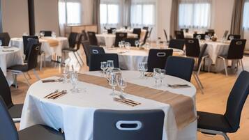 A conference room with round tables, black chairs, and white tablecloths.