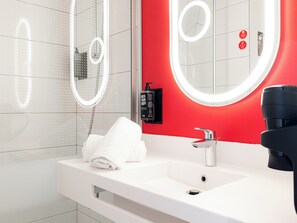 Une salle de bain moderne avec un lavabo blanc, un mur d’accent rouge et un grand miroir doté d’un anneau lumineux.