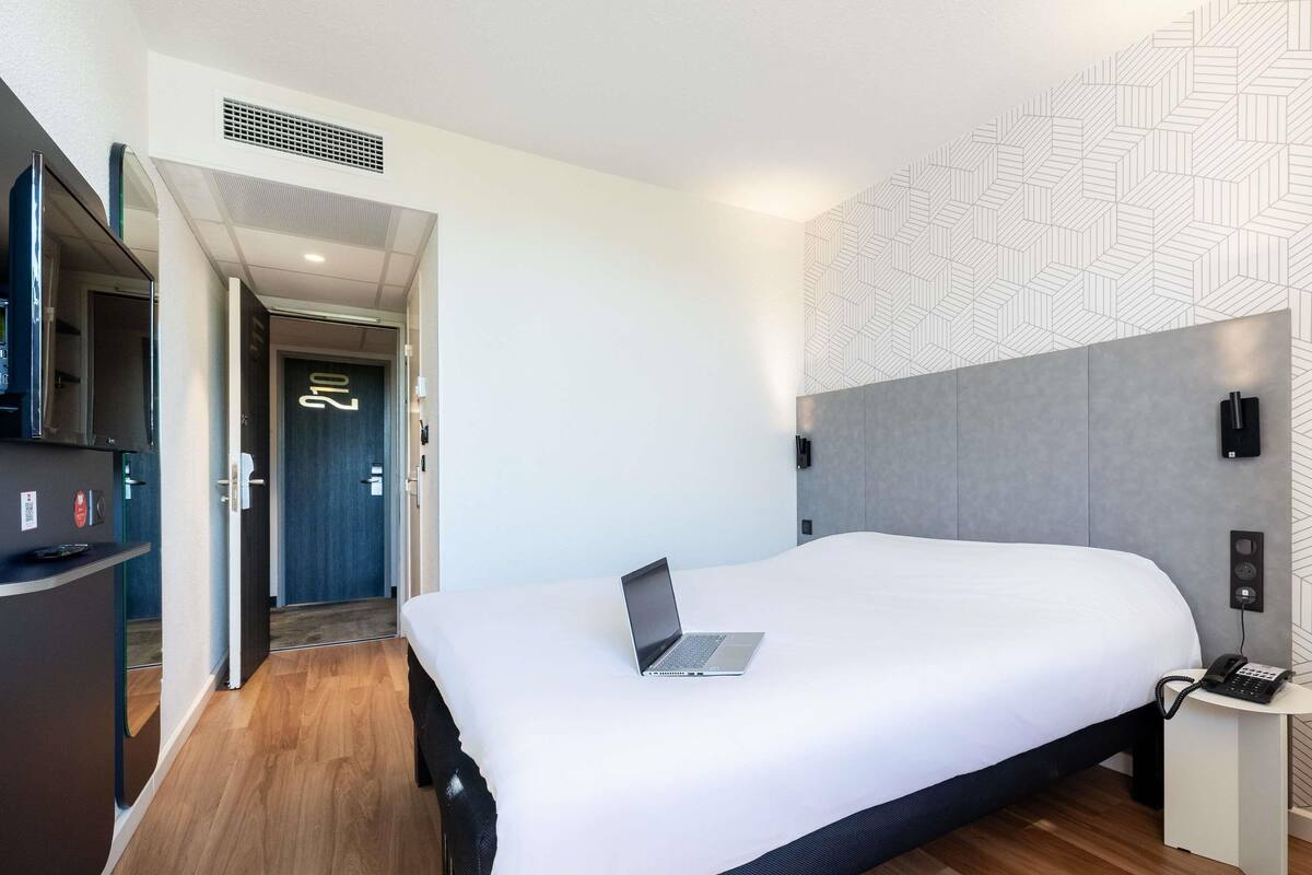 Une chambre d’hôtel moderne avec un grand lit, un bureau avec un ordinateur portable, un téléphone et une télévision.