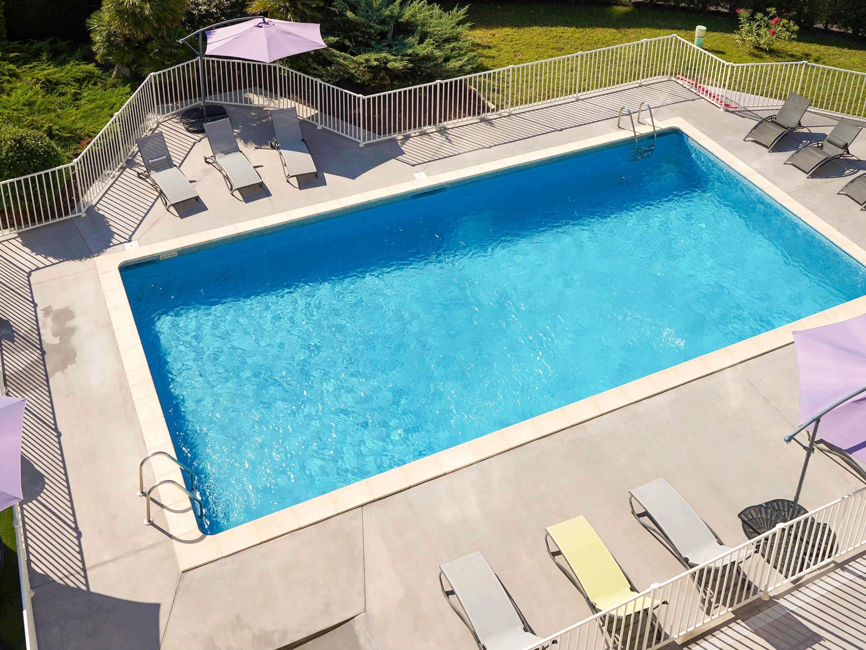 A rectangular swimming pool with a white deck, surrounded by a white metal fence.