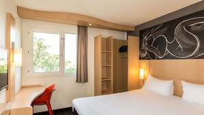 Una habitación de hotel con cama, escritorio, silla, armario y ventana con cortinas.