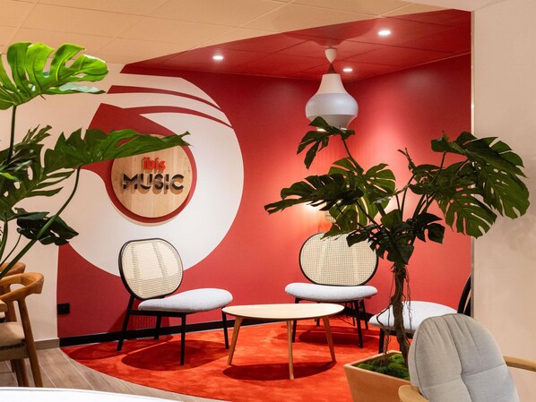 A modern interior with two wicker chairs, a small table, and large green plants. - Hôtel ibis Beziers Est Mediterranee (Villeneuve-les-Beziers)
