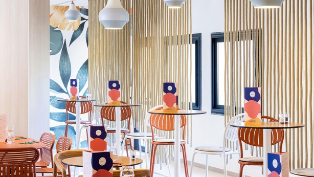 Un espace de restauration moderne avec des tables rondes, des chaises orange et des lambris en bois verticaux.