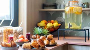 A breakfast buffet with pastries, fruits, and a fruit-infused drink.
