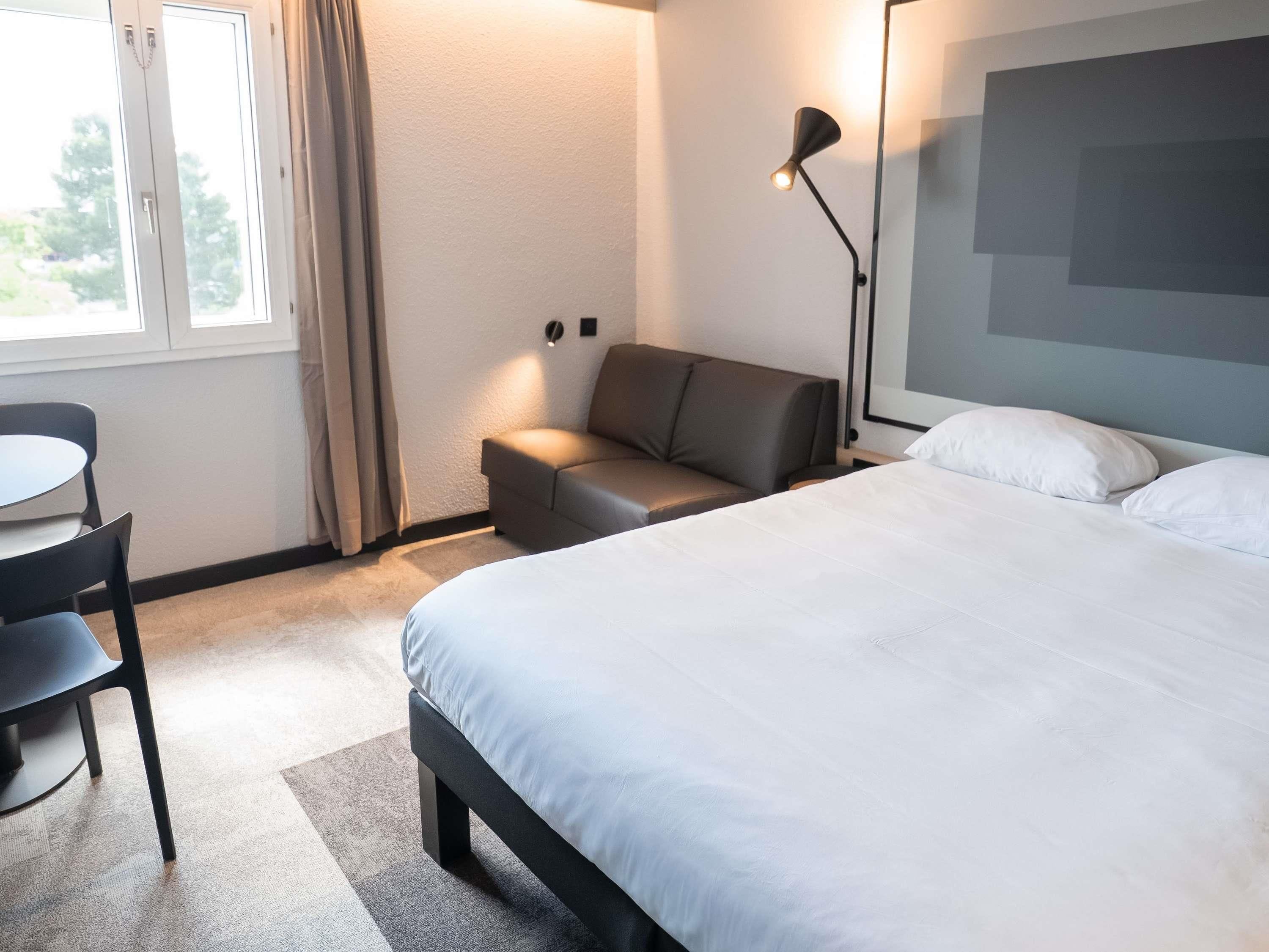 A hotel room with a bed, a sofa, a desk, and a lamp.