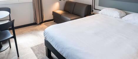 A hotel room with a bed, a sofa, a desk, and a lamp.
