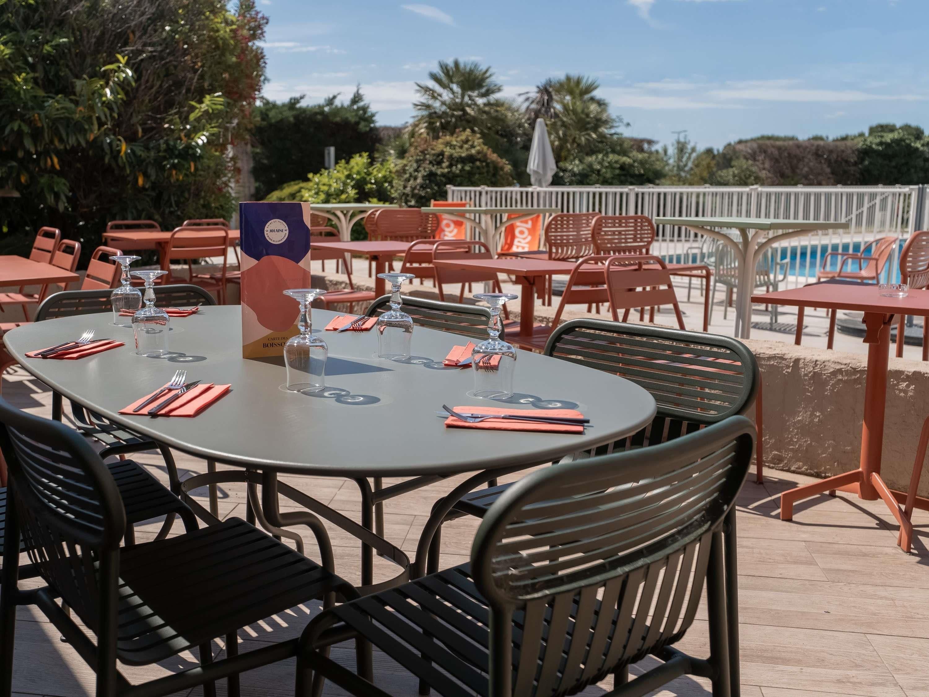 An outdoor dining area with round tables, metal chairs, and clear glassware.
