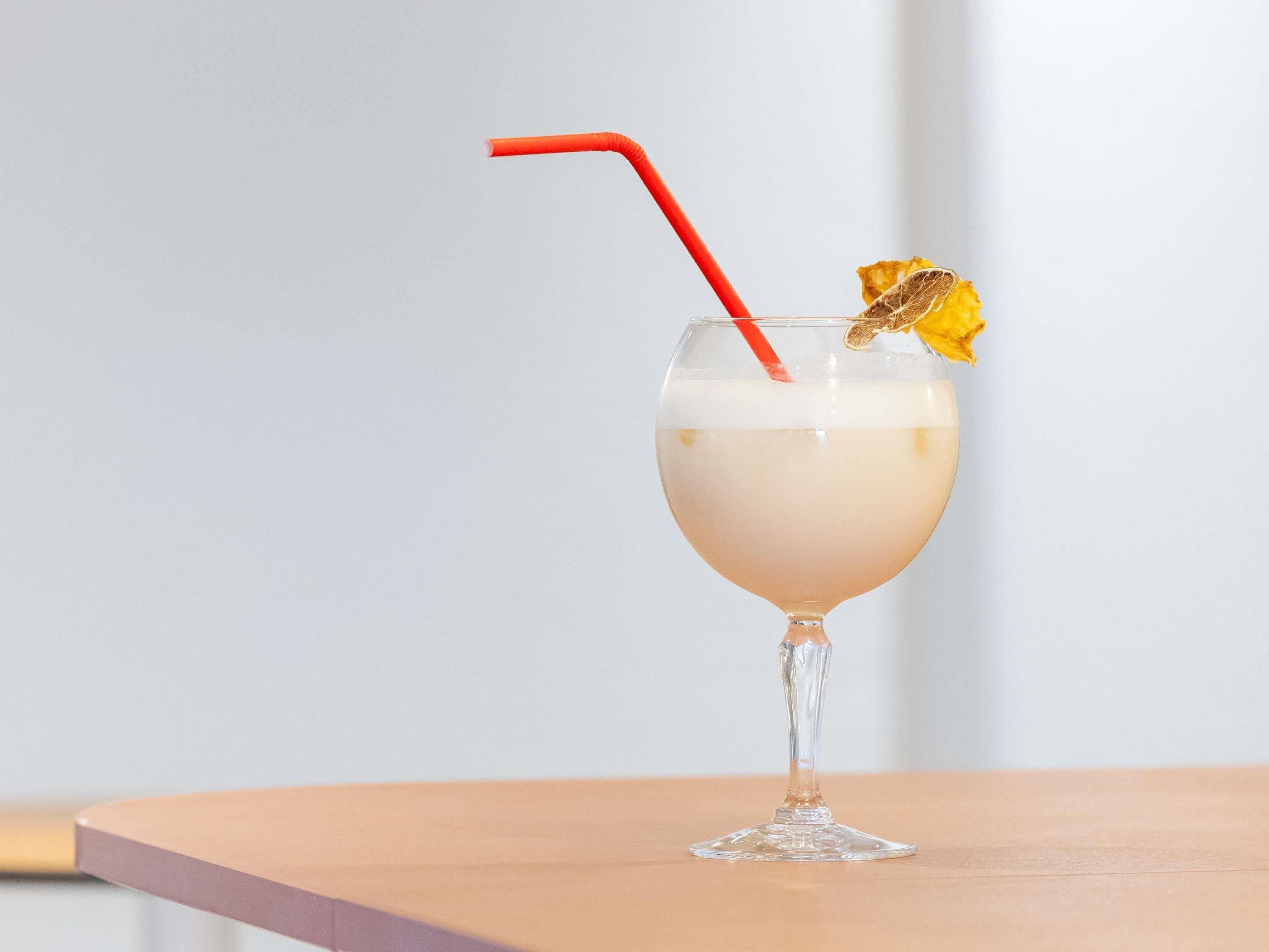 Un cocktail servi dans un verre à pied, agrémenté d’une tranche d’orange séchée et d’une paille rouge.
