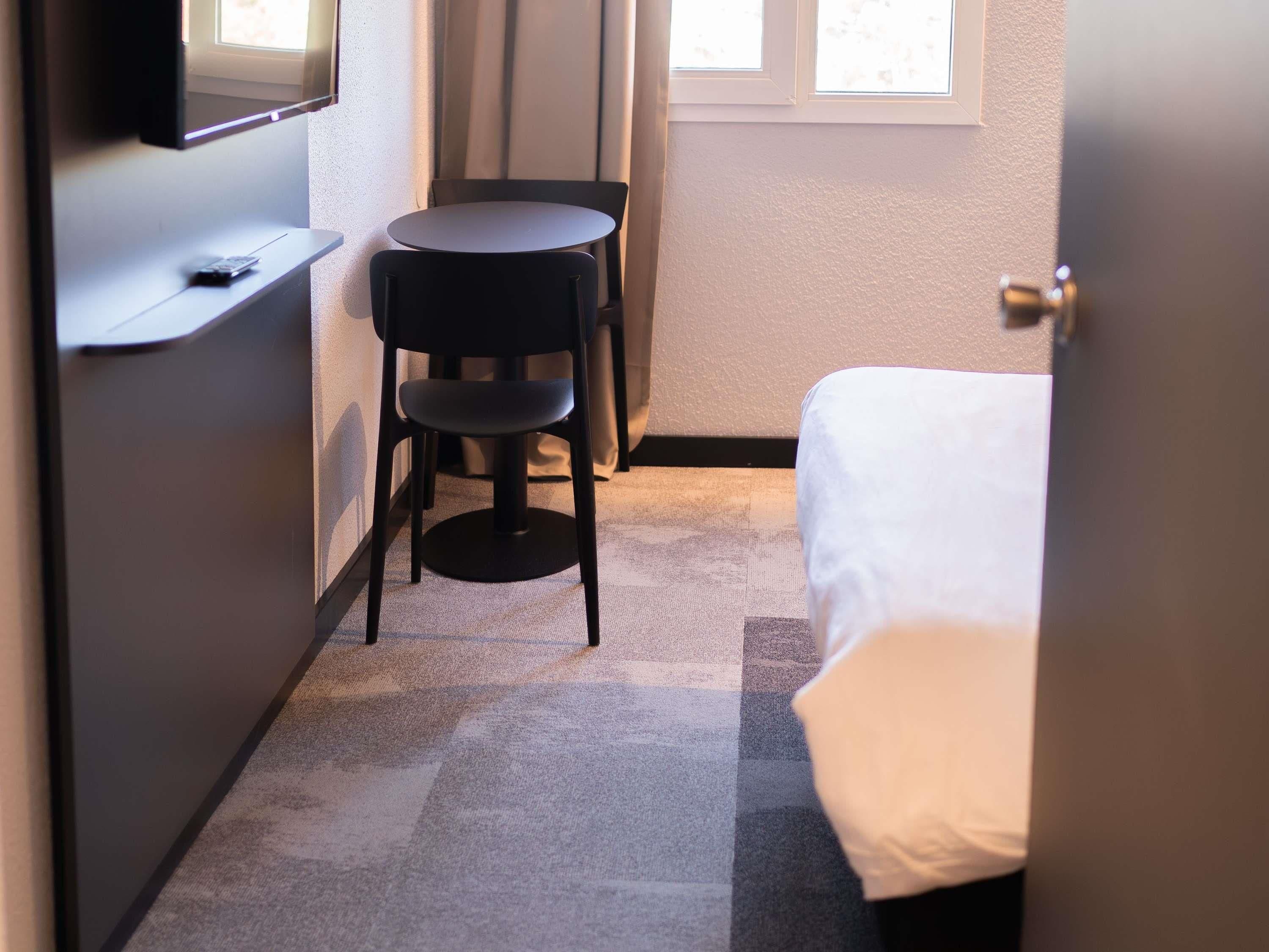 Una habitación pequeña con cama, una silla, una mesa, un televisor y una ventana.