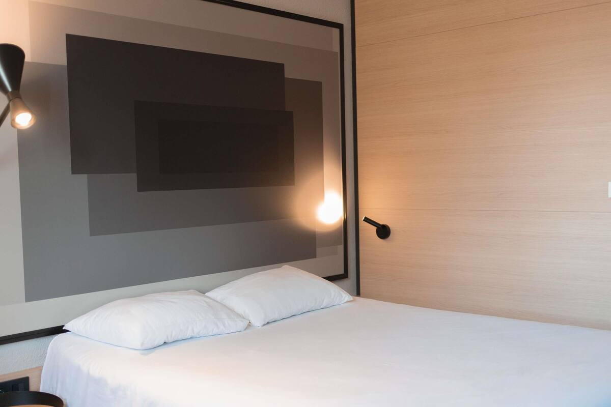 Une chambre d’hôtel moderne avec un grand lit, une table de chevet et un luminaire fixé au mur.