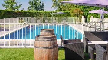 Ein Schwimmbecken mit einem Holzfass, Korbmöbeln und Sonnenschirmen.