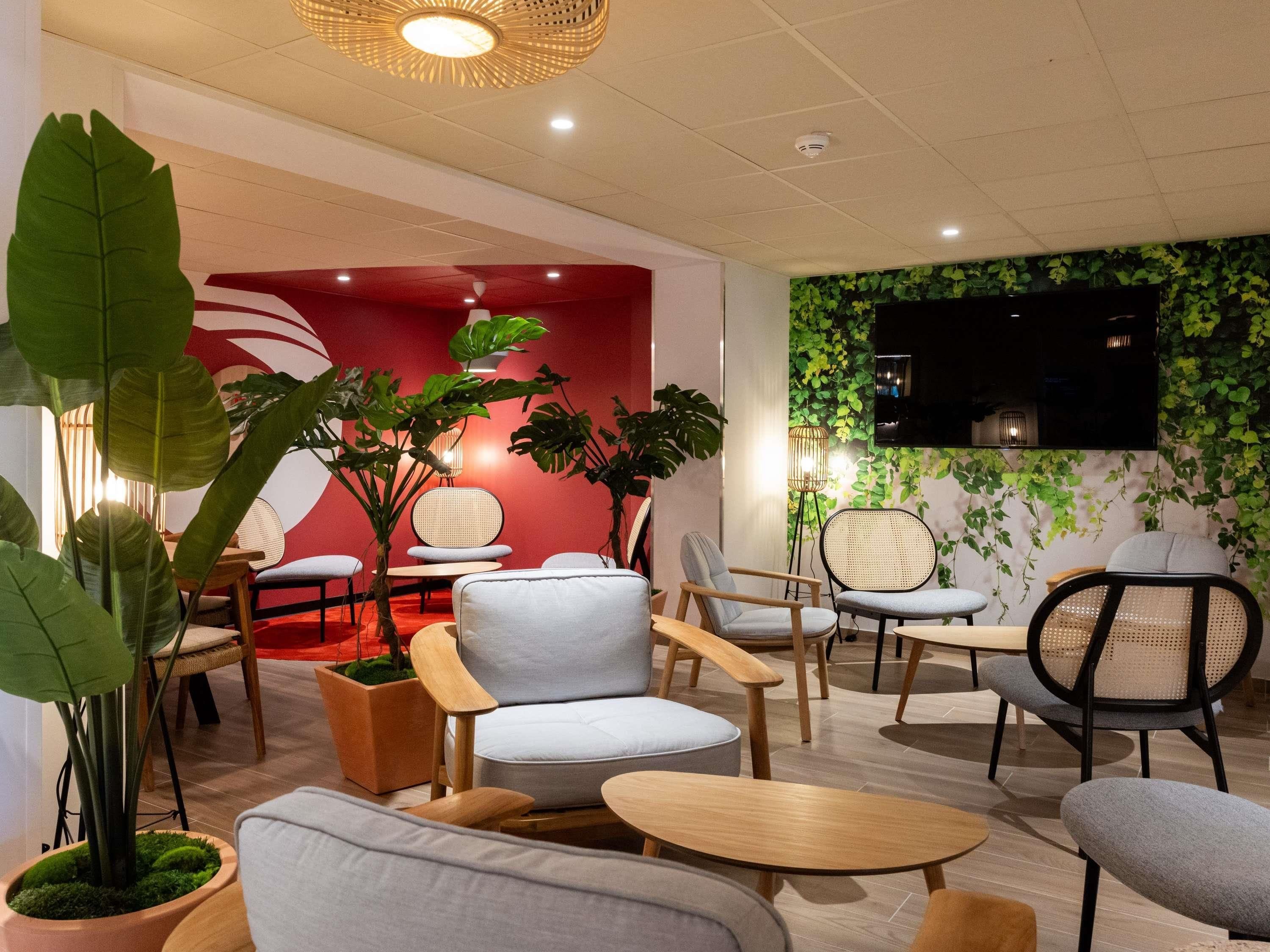A modern lounge area with seating arrangements, potted plants, and a wall-mounted TV.