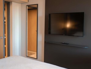Habitación de hotel con cama, armario, espejo, televisor montado en la pared y control remoto sobre la cama.