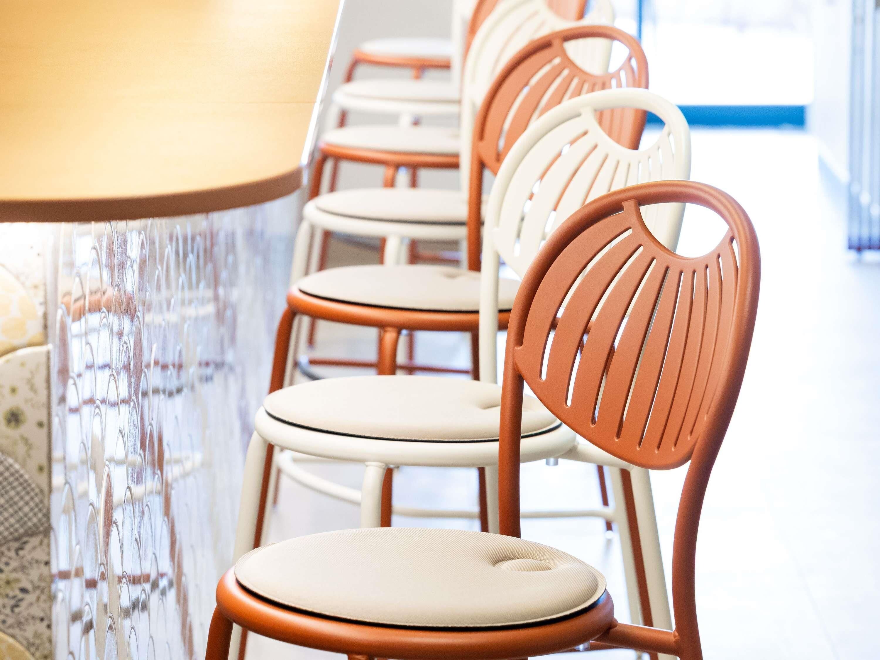 A row of chairs with a round table, a patterned wall, and a window with blinds.