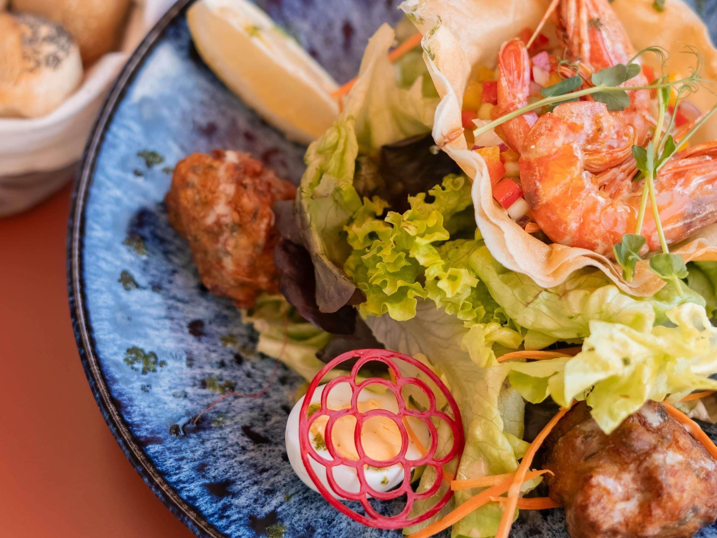Un plato con ensalada, camarones y albóndigas.
