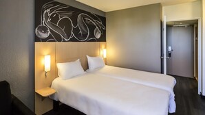 Una habitación de hotel con una cama grande, dos lámparas de noche, una obra de arte en la pared y una puerta a la derecha.