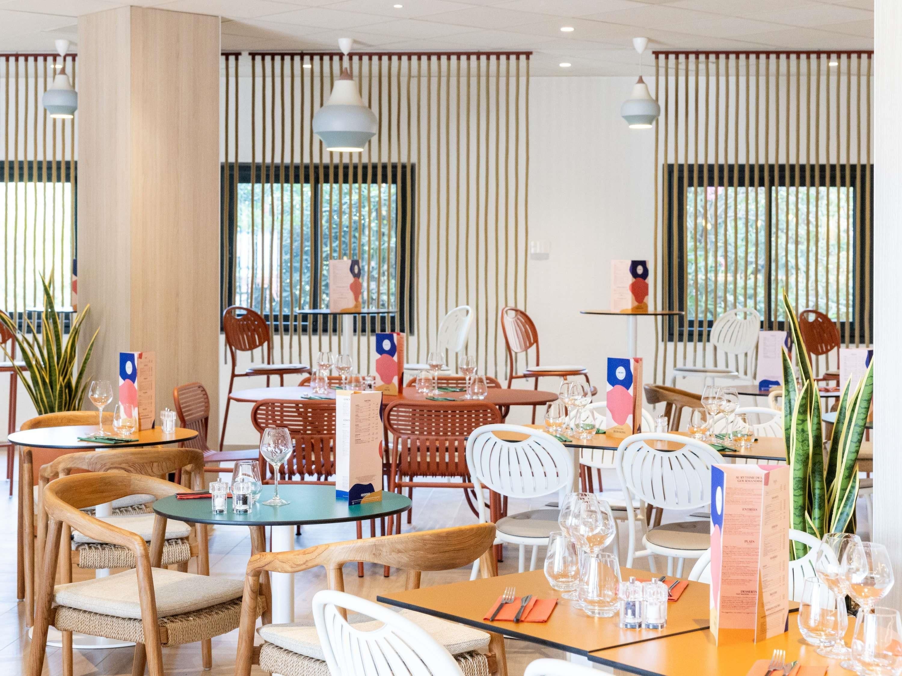 A restaurant interior with wooden chairs, round tables, and hanging pendant lights.