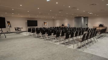A conference room with rows of chairs, a projector screen, a presentation screen, and a water dispenser.