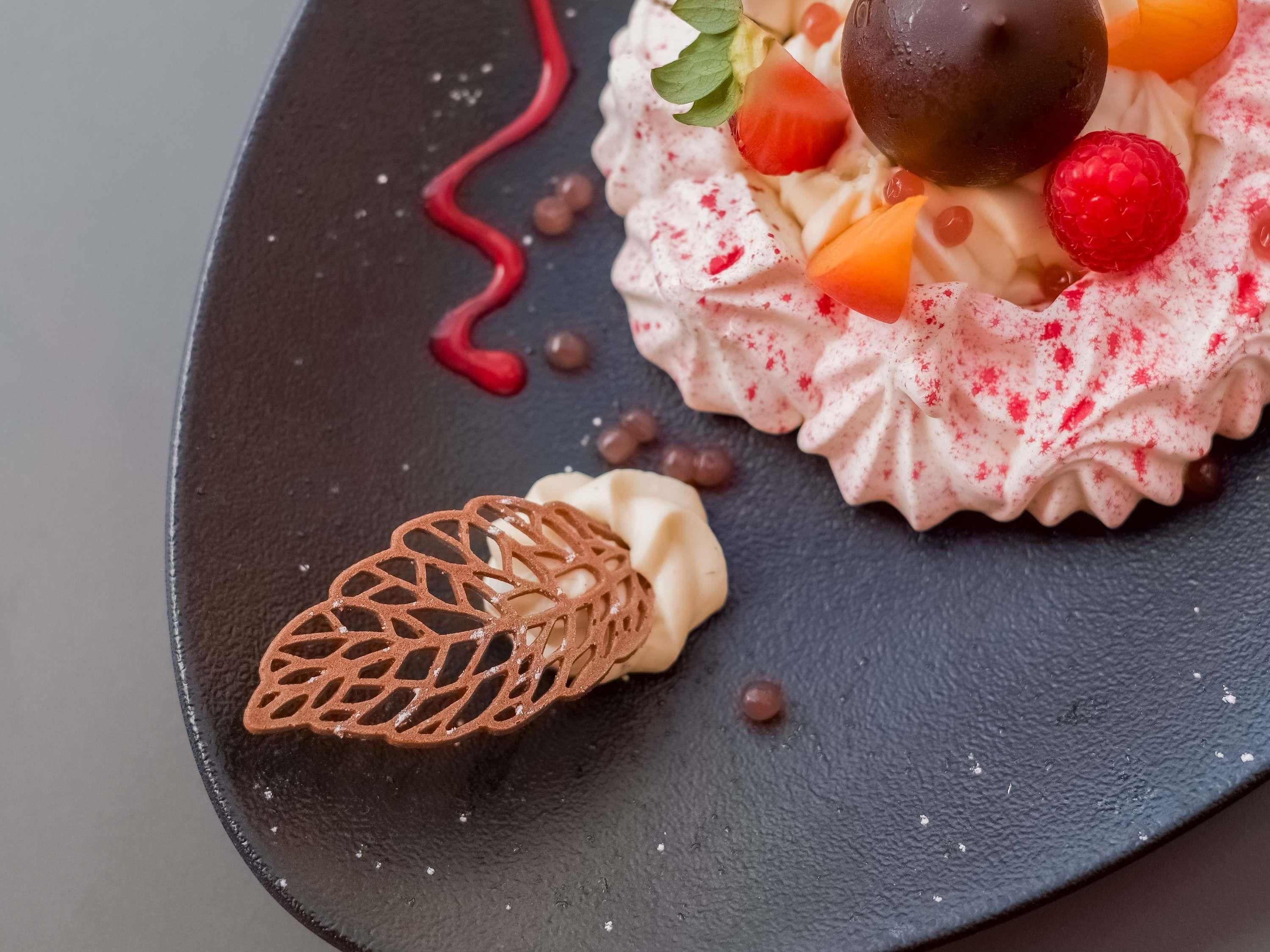 Un postre con fresas, una esfera de chocolate y un adorno sobre un plato oscuro.
