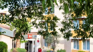A hotel entrance with a sign reading "ibis Hotels", surrounded by greenery and a clear sky. - Hôtel ibis Beziers Est Mediterranee (Villeneuve-les-Beziers)