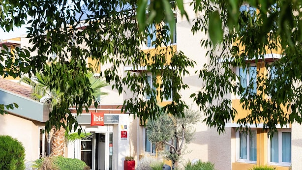 Entrada de un hotel con un cartel que dice "ibis Hotels", rodeada de follaje y un cielo despejado.