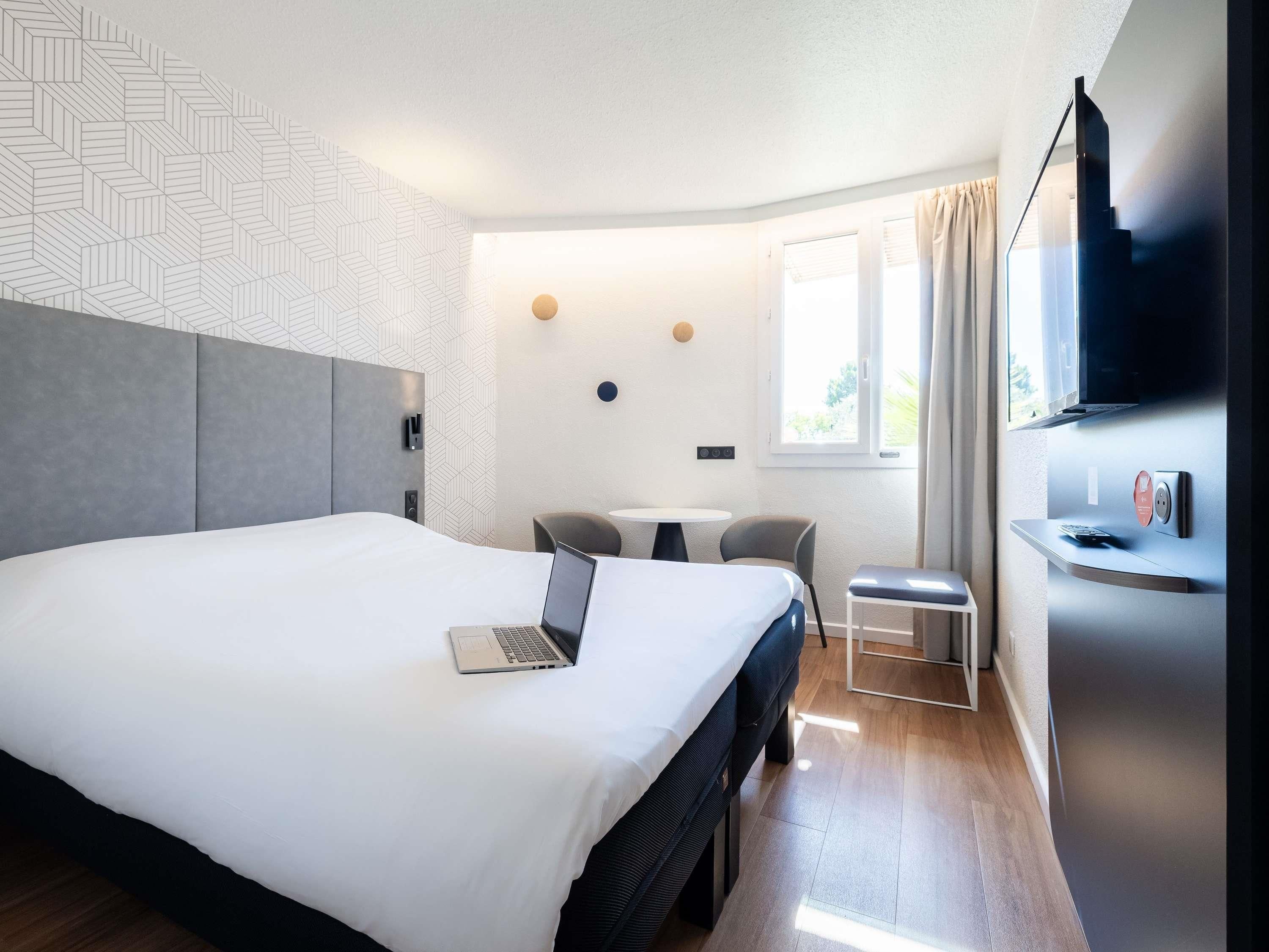 Una habitación de hotel moderna con una cama grande, un escritorio, una silla, un televisor y un ventanal con cortinas.