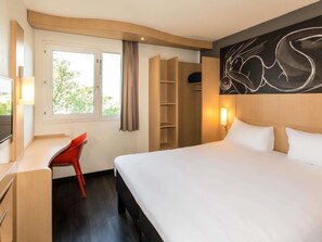 Ein Hotelzimmer mit Bett, Schreibtisch, Stuhl, Kleiderschrank und einem Fenster mit Vorhängen.