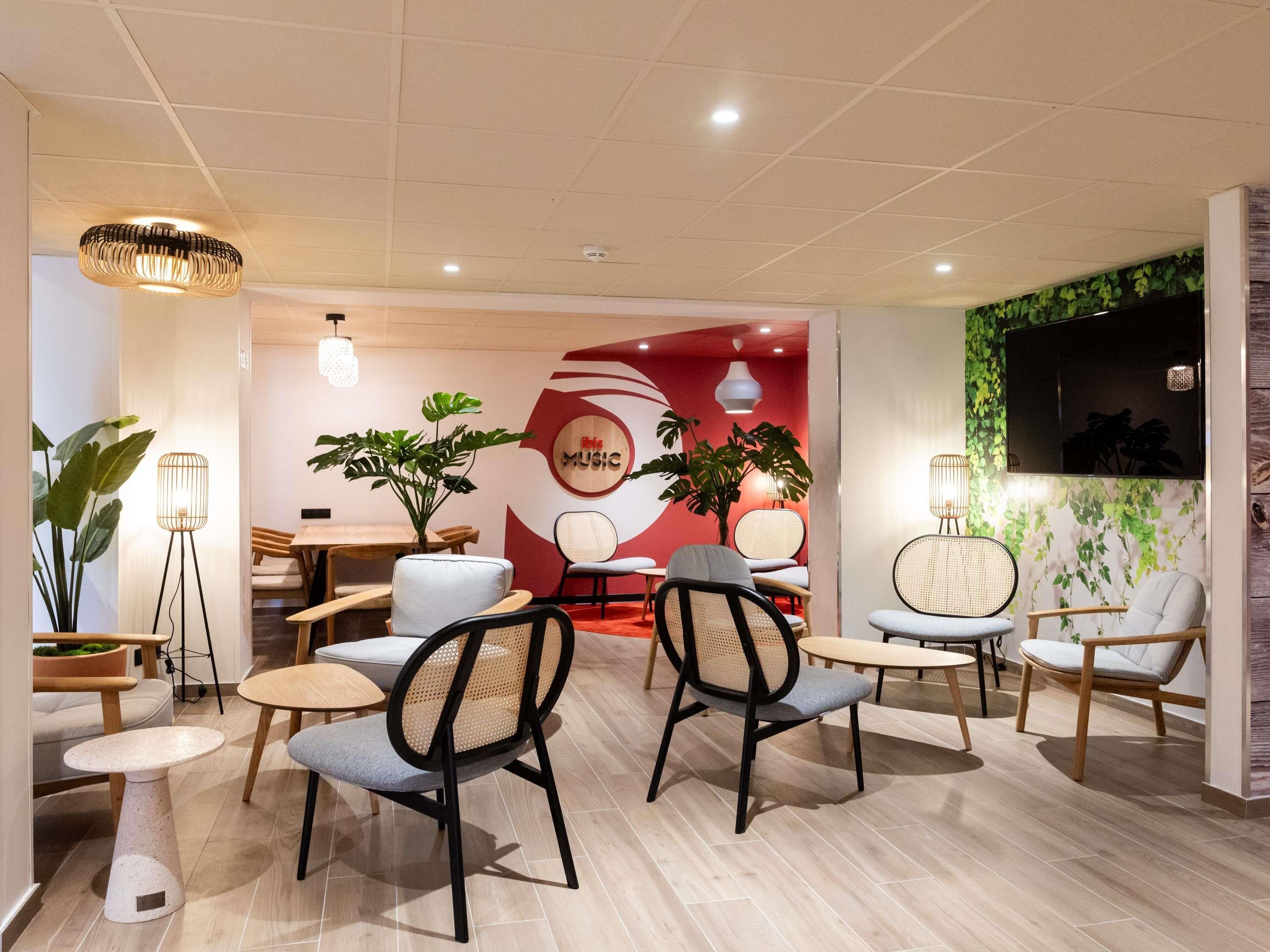 A modern interior with seating areas, a wall with a 'MUSIC' sign, and a television mounted on a green leafy wall.